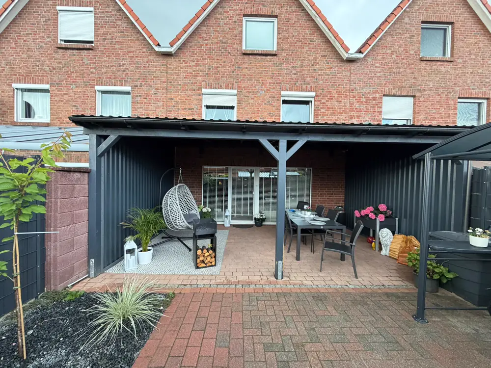 Gepflasterte Terrasse mit Überdachung und Sitzbereich hinter einem Wohnhaus
