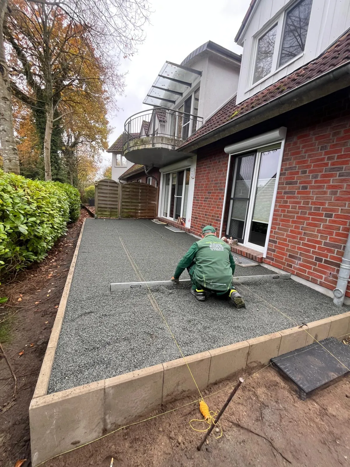 Mitarbeiter in Arbeitskleidung von Garten Team Krause zieht das Splittbett für eine Terrasse ab