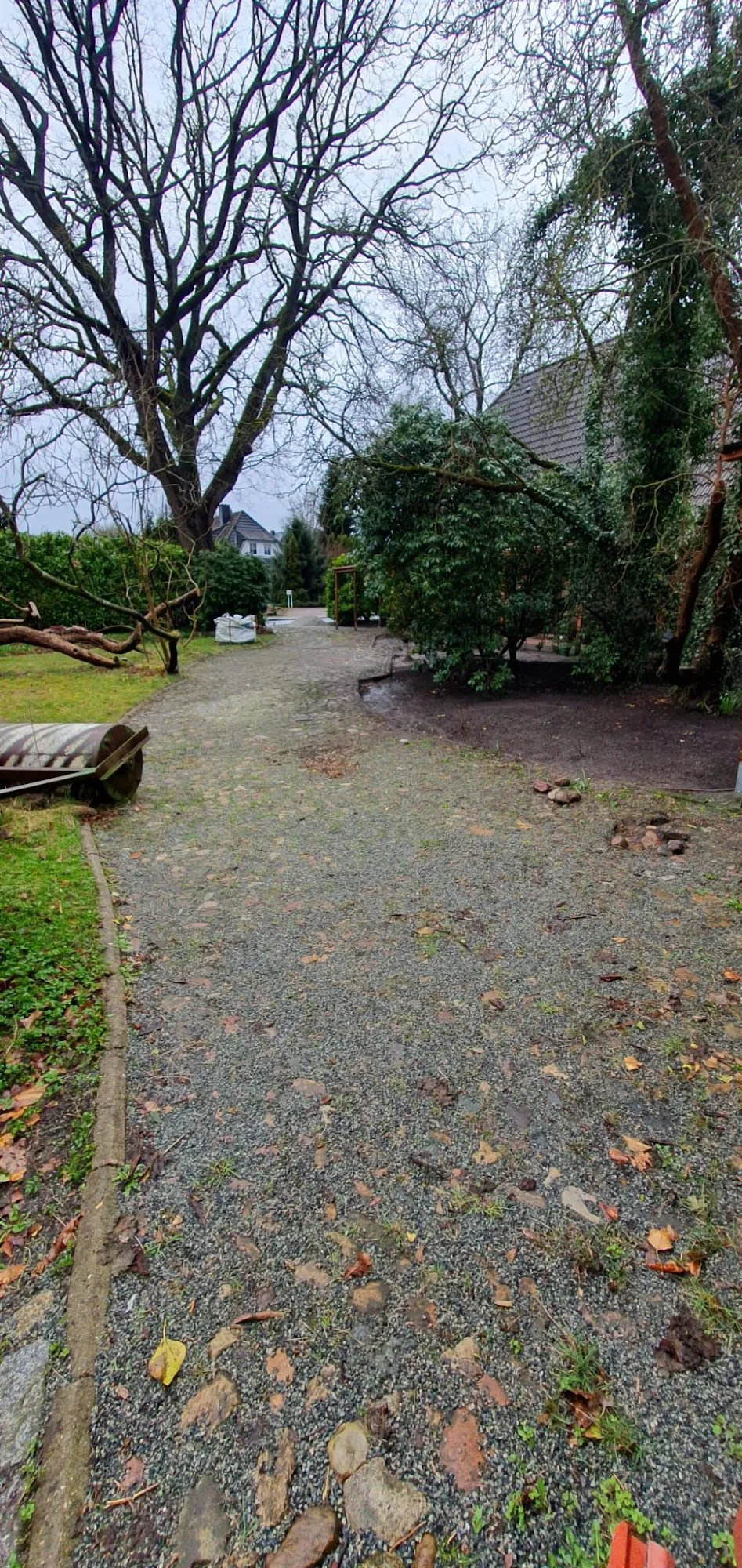 Zufahrt aus Schotter und Erde vor Beginn der Pflasterarbeiten, daneben eine Gartenwalze